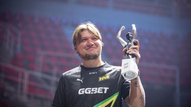 S1mple, un giocatore di Counter-Strike, indossa una maglia NAVI e solleva un trofeo in uno stadio.